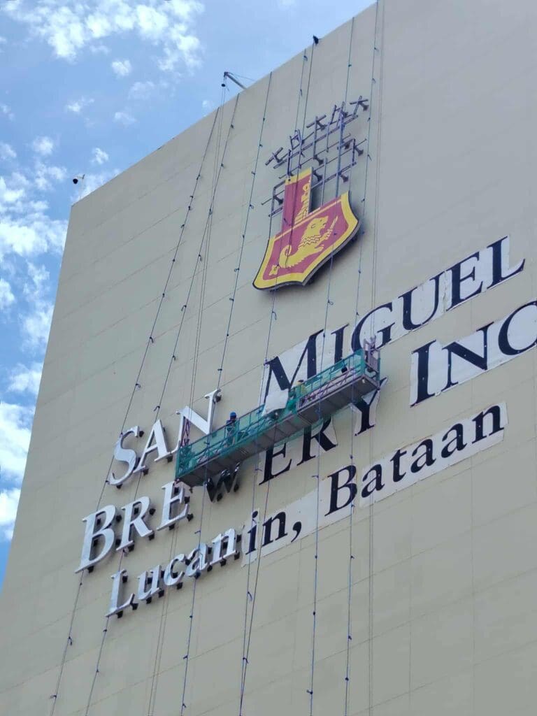 Workers clean San Miguel Brewery outdoor building signage in Lucanin, Bataan. Sign maker Philippines by M&G Global Ads.