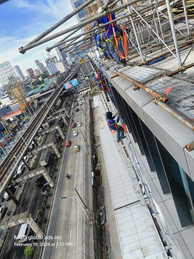 Workers in safety gear on ropes clean building exterior, outdoor signage visible, Metro Manila sign maker Philippines by M&G Global Ads.