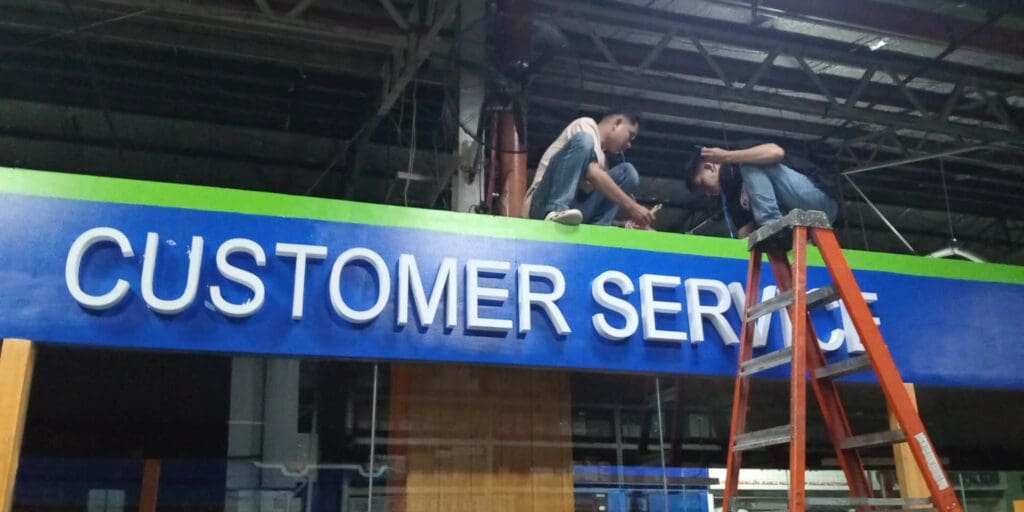 Workers installing acrylic CUSTOMER SERVICE indoor signage, Metro Manila, sign maker Philippines by M&G Global Ads.